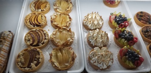 A display of assorted pastries, including fruit tarts with meringue, almond topping, and various fruit decorations.