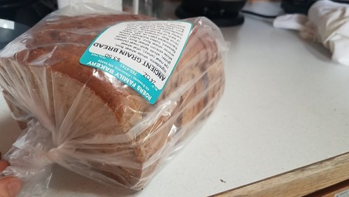 A loaf of whole grain bread in a clear plastic bag on a kitchen countertop.