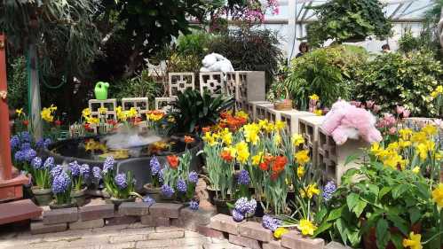 A vibrant garden with colorful flowers, a small pond, and plush toys nestled among the plants.