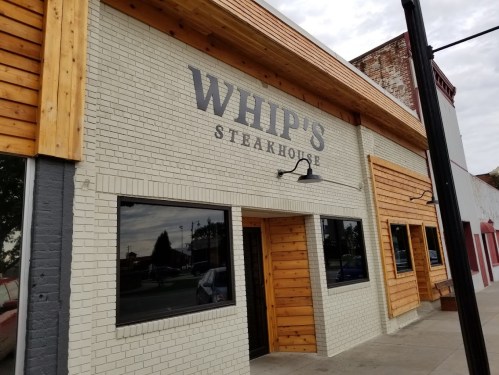 Exterior of Whip's Steakhouse, featuring a brick facade and wooden accents, with large windows and a sign above the entrance.