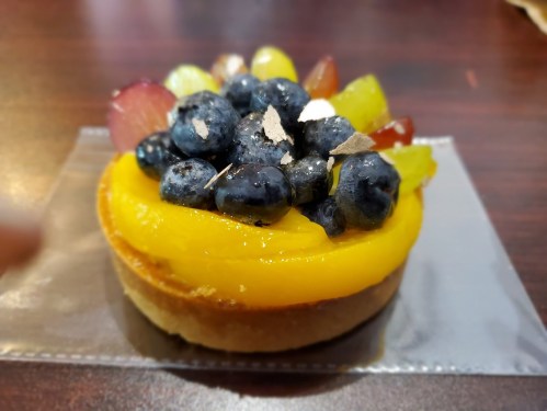 A colorful fruit tart topped with blueberries, grapes, and a layer of yellow mango filling on a pastry crust.