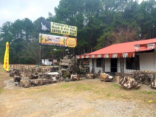 A rock and gift shop with a sign, surrounded by trees and featuring decorative rocks in front.