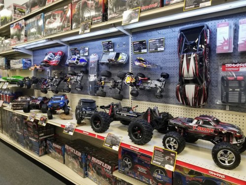 A display of various remote-controlled cars and trucks on shelves in a store, with boxes and accessories visible.