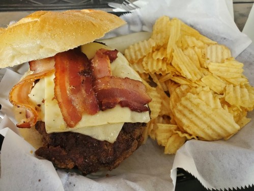A juicy burger topped with melted cheese and crispy bacon, served with a side of ridged potato chips.