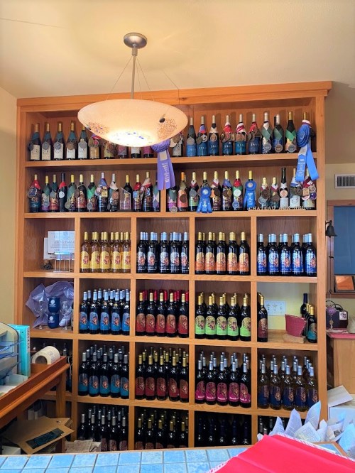 A wooden shelf displaying various bottles of wine and awards, with a decorative light fixture above.