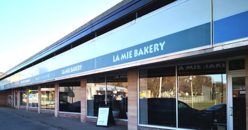 Exterior of La Mie Bakery, featuring large windows and a blue and white sign, in a commercial building.