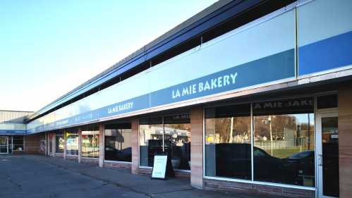 Exterior of La Mie Bakery, featuring large windows and a blue sign, in a shopping plaza on a clear day.