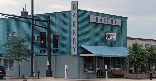 A teal building with a sign reading "BAKERY" and a blue awning, located at an intersection with traffic lights.