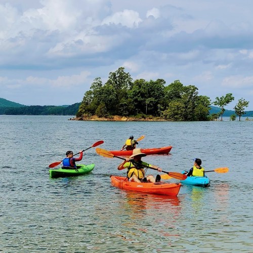 A group of people kayaking on a calm lake with an island in the background and cloudy skies above.