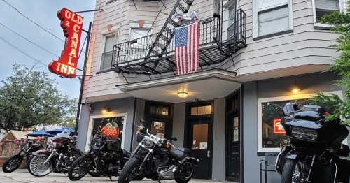 Exterior of the Old Canal Inn with a large American flag, surrounded by parked motorcycles and evening lighting.
