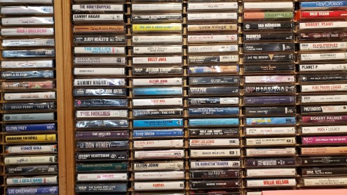 A wall of cassette tapes organized by artist, featuring various music genres and notable musicians.