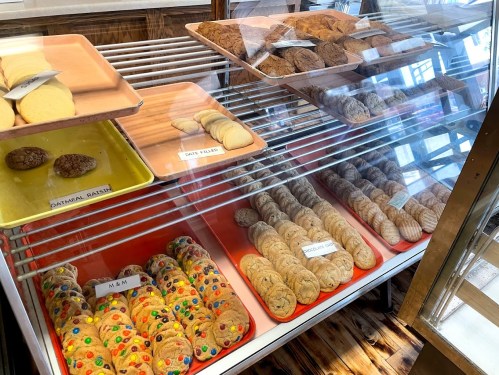 A display case filled with various cookies, including oatmeal raisin, M&M, and chocolate chip varieties.