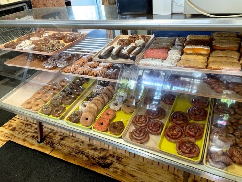A display case filled with various donuts, including glazed, frosted, and sprinkled varieties, arranged on trays.