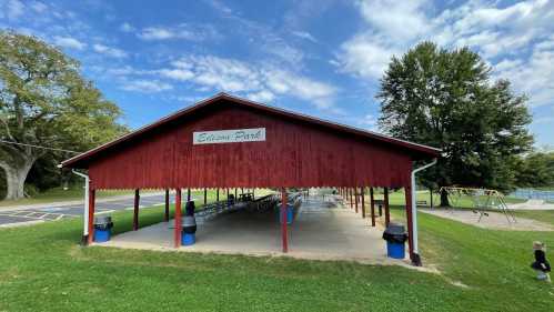 A red pavilion at Edison Park with picnic tables, surrounded by green grass and trees under a blue sky.