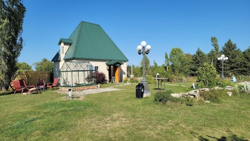 A quaint house with a green roof, surrounded by a garden and outdoor seating, under a clear blue sky.