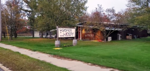 Sign for Yooper Winery with "Wine Tasting" displayed, surrounded by trees and a grassy area.