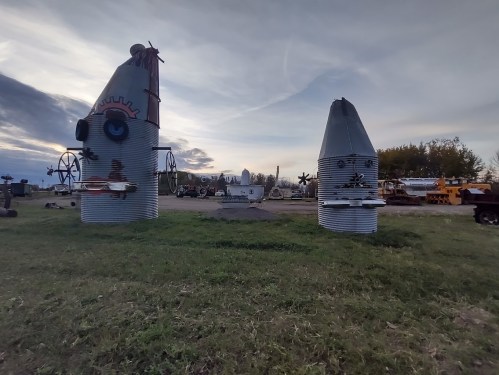 Two large, whimsical metal sculptures resembling rockets, set in a grassy area with a cloudy sky in the background.