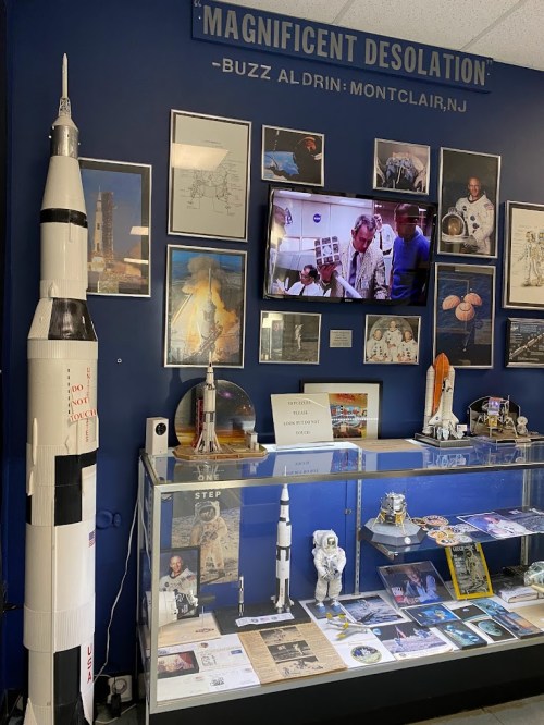 Display featuring models of rockets, astronaut memorabilia, and a TV showing historical space footage, with a blue background.