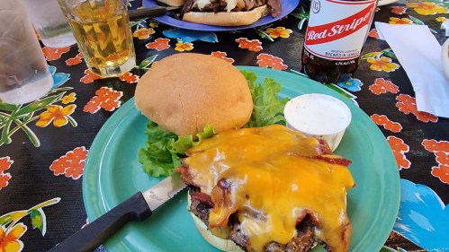 A juicy cheeseburger topped with bacon and melted cheese, served with a side of ranch dressing on a colorful floral table.