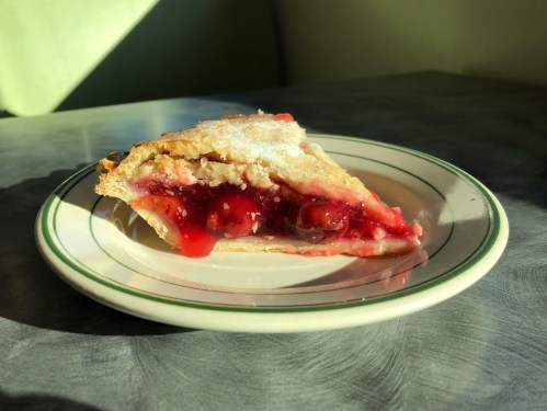 A slice of cherry pie on a white plate, showcasing a glossy red filling and a golden, flaky crust.