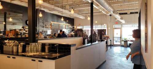 A modern café interior with patrons, large windows, and industrial lighting, featuring a counter and seating area.