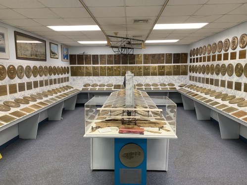 A museum room filled with plaques and displays, featuring a model airplane at the center and historical aviation memorabilia.