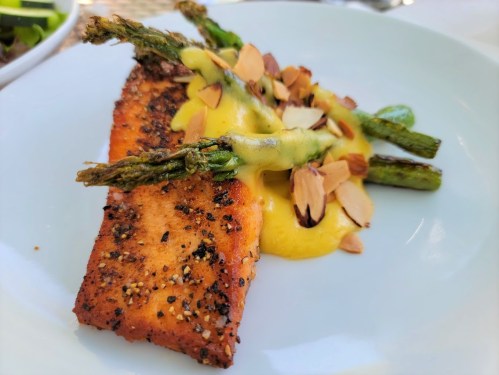 A plate featuring a seasoned salmon fillet topped with asparagus and almond slices, drizzled with a creamy sauce.