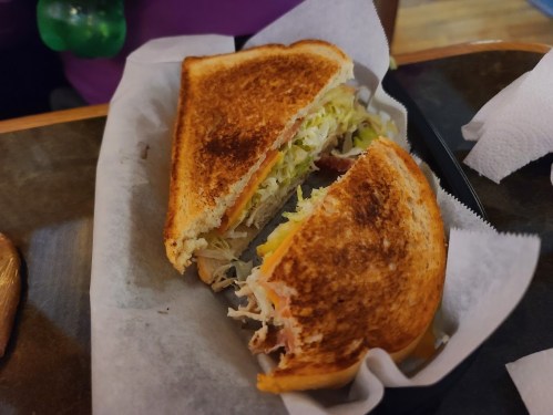 A toasted sandwich filled with shredded lettuce and meat, served on a paper-lined plate.