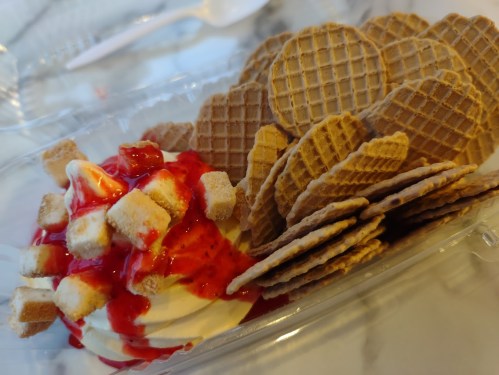 A dessert featuring soft-serve ice cream topped with strawberry sauce and crunchy wafer cookies.