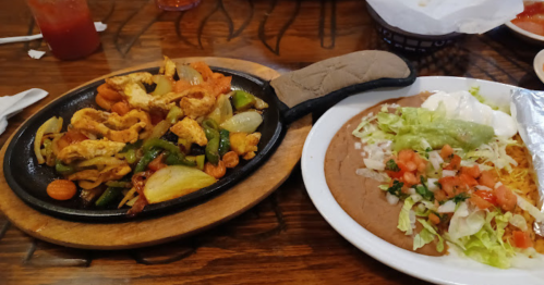 A sizzling platter of chicken fajitas with peppers and onions, alongside a plate of refried beans and a fresh salad.