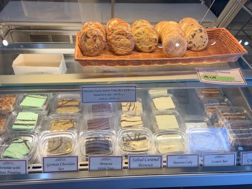 Display case filled with various desserts, including cookies, brownies, and bars, with prices listed.