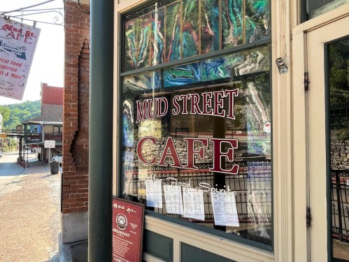 A cafe window displaying "Mud Street Cafe" with colorful reflections and menus posted on the glass.