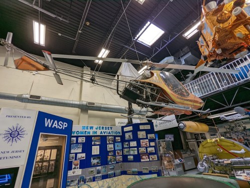A helicopter and various aircraft models displayed in an aviation museum, with informational panels in the background.