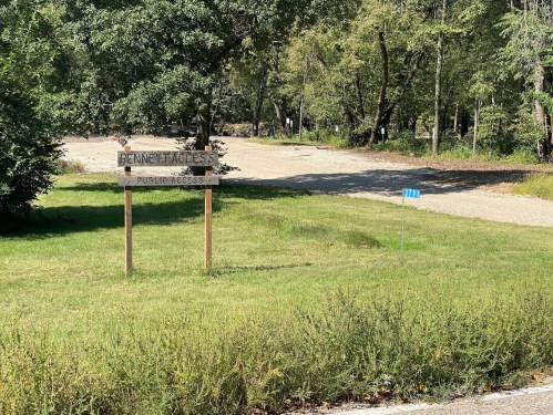 A wooden sign reading "Bennett Access" stands near a gravel road, surrounded by trees and grassy areas.