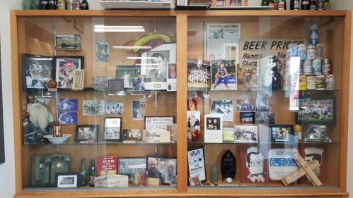 Display case filled with sports memorabilia, photos, trophies, and vintage items, showcasing local history and achievements.