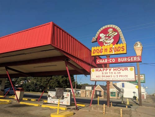 A retro fast-food restaurant sign for "Dog n Suds" featuring a cartoon dog and announcing a happy hour special.