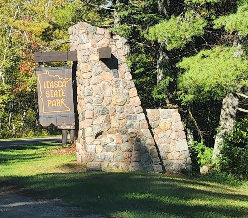 Sign for Itasca State Park, featuring a stone structure surrounded by trees and greenery.