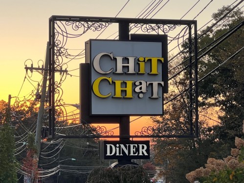Sign for "Chit Chat Diner" against a sunset backdrop, with power lines in the foreground.