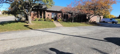 A brick building with a landscaped front yard, featuring trees and autumn foliage, on a sunny day.