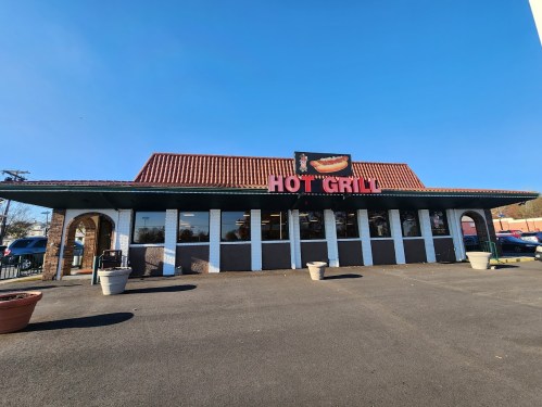 Exterior of a restaurant named "Hot Grill," featuring a red roof and large windows under a clear blue sky.