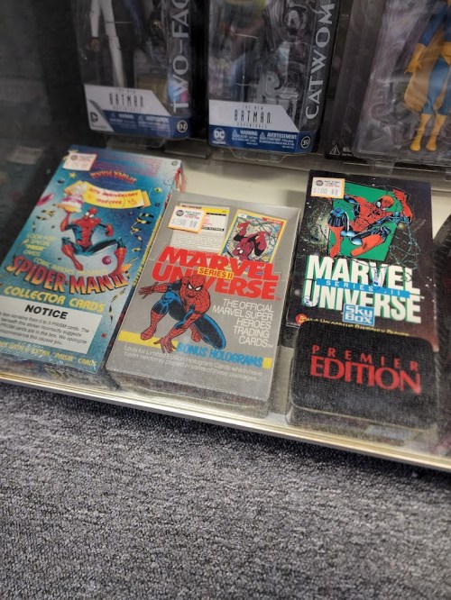 Display of Marvel trading card packs, including Spider-Man and Marvel Universe, in a glass case.