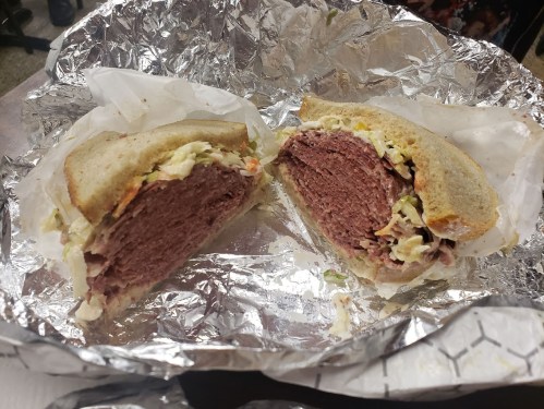 A cut sandwich with layers of meat and coleslaw, wrapped in foil, showcasing its filling and fresh bread.