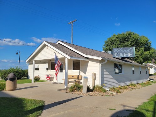 A small white café building with an American flag, surrounded by greenery and a clear blue sky.