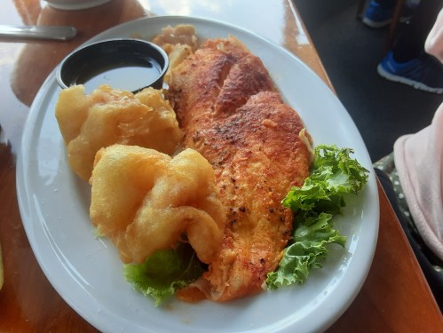 A plate featuring a golden omelet, crispy fried dough, and a side of lettuce, with a small cup of dipping sauce.
