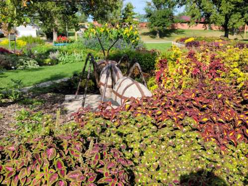 A large insect sculpture surrounded by colorful flowers and greenery in a garden setting.