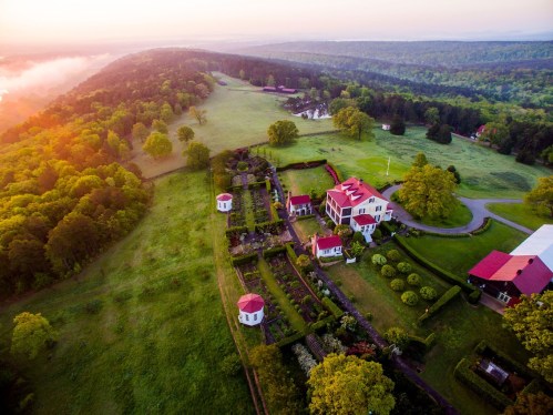 Aerial view of a sprawling estate with gardens, red-roofed buildings, and lush green landscapes at sunrise.