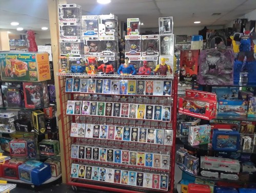 A display of various collectible figurines and toys on shelves, surrounded by colorful boxes and games.