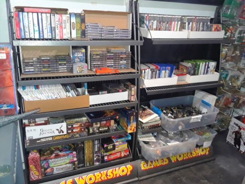 A shelf filled with various video games, board games, and collectibles, organized in boxes and containers.