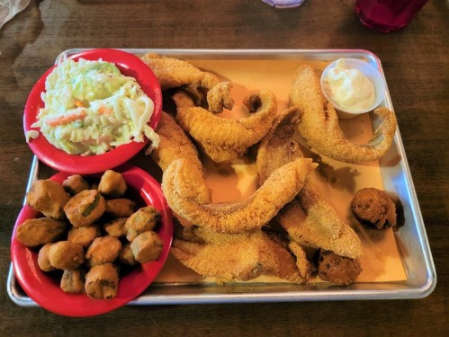 A metal tray with fried catfish, coleslaw, hushpuppies, and a side of dipping sauce.
