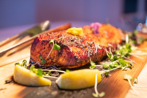 Grilled salmon fillet garnished with lemon wedges and microgreens on a wooden platter.